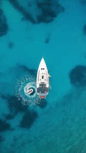 A luxury yacht anchored in clear turquoise water with a small dinghy circling nearby.