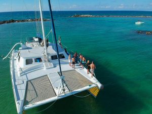 Group of guests relaxing on a luxury catamaran during a snorkeling boat tour in Playa del Carmen, Mexico, anchored in clear turquoise Caribbean water.