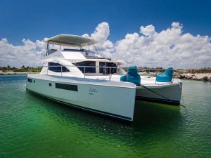 Luxury catamaran yacht anchored in clear green water in Playa del Carmen, Mexico, available for private boat rental and snorkeling tours.
